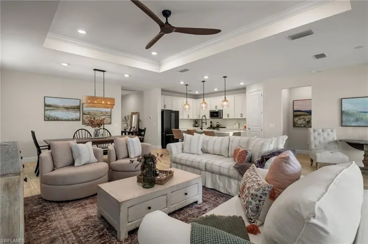 Living room featuring light wood-look tile flooring, a raised ceiling, crown molding, and ceiling fan