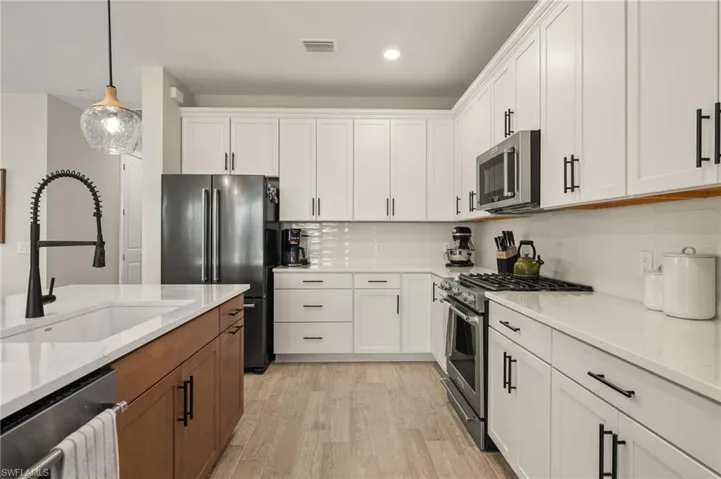 Kitchen featuring sink, light stone countertops, decorative light fixtures, white cabinetry, and stainless steel appliances