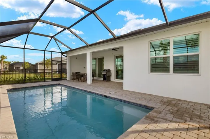 View of pool featuring glass enclosure, ceiling fan, a patio, and grilling area