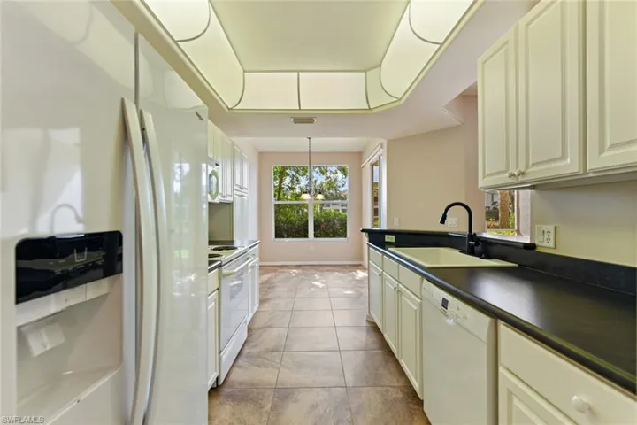 Kitchen with a tray ceiling, a sink, light tile patterned floors, white appliances, and dark countertops