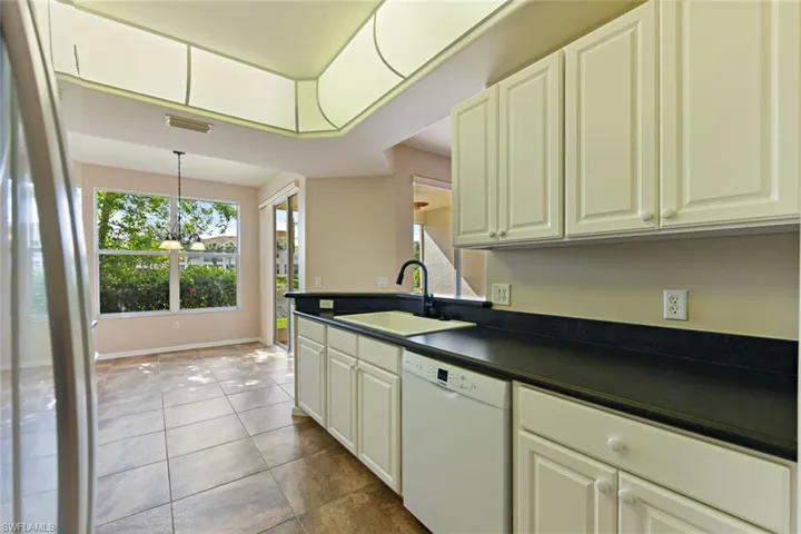 Kitchen with dark countertops, a sink, white dishwasher, and a wealth of natural light
