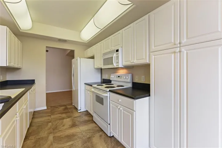 Kitchen with visible vents, white appliances, baseboards, dark countertops, and white cabinetry