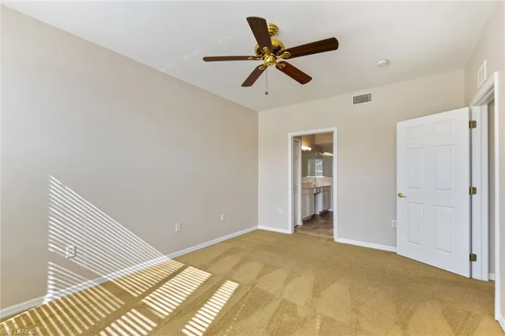 Unfurnished bedroom featuring light carpet, baseboards, visible vents, and ensuite bathroom