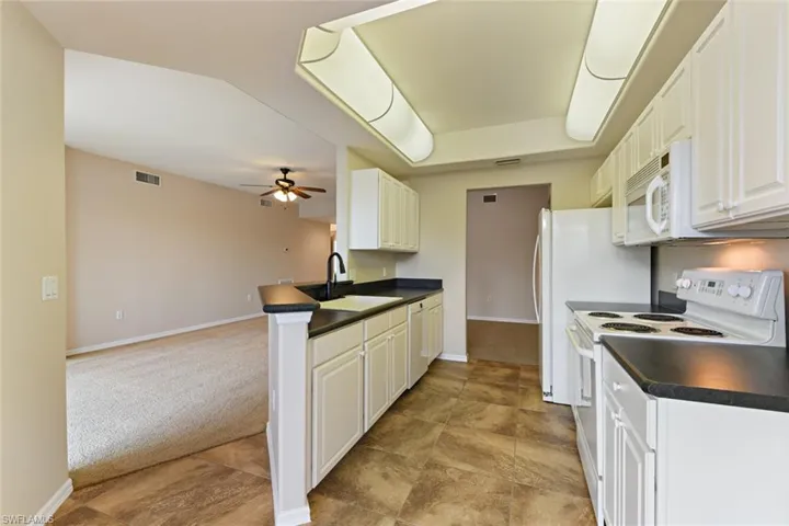 Kitchen featuring a sink, light carpet, white appliances, dark countertops, and ceiling fan