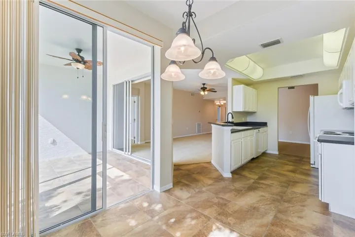Kitchen with a sink, white dishwasher, dark countertops, decorative light fixtures, and ceiling fan