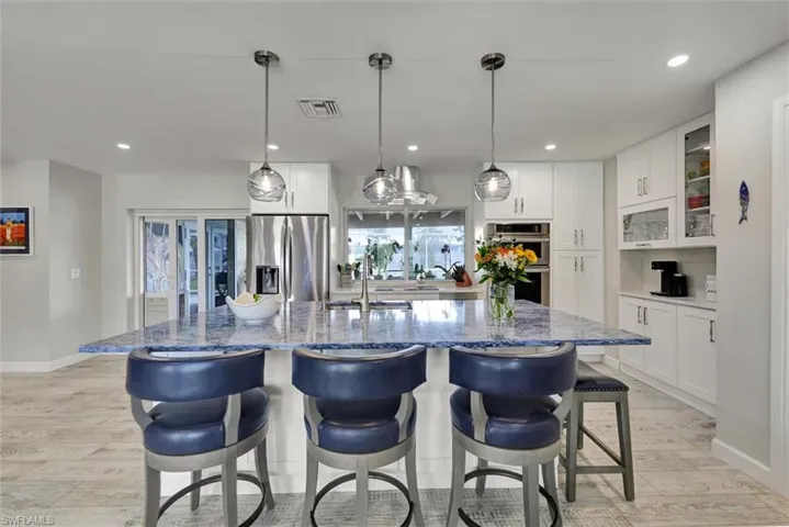 Kitchen featuring white cabinets, visible vents, appliances with stainless steel finishes, a kitchen island with sink, and light stone counters