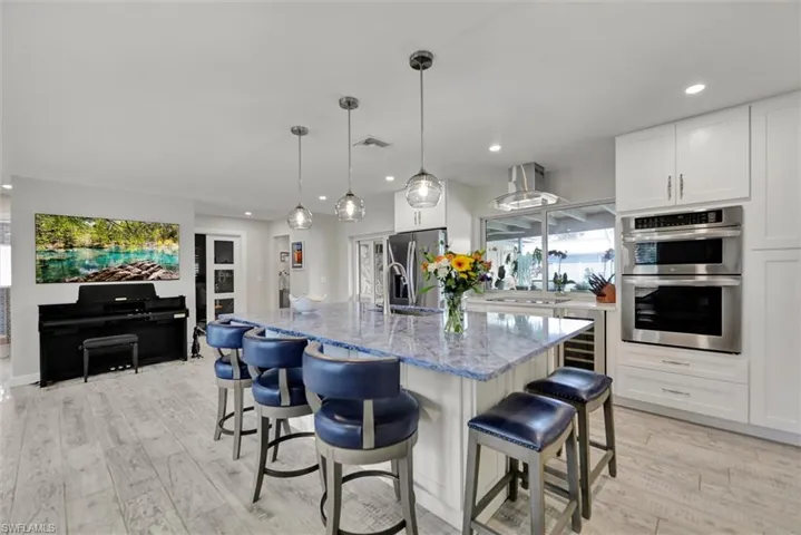 Kitchen with a breakfast bar, light stone counters, visible vents, wine cooler, and stainless steel appliances