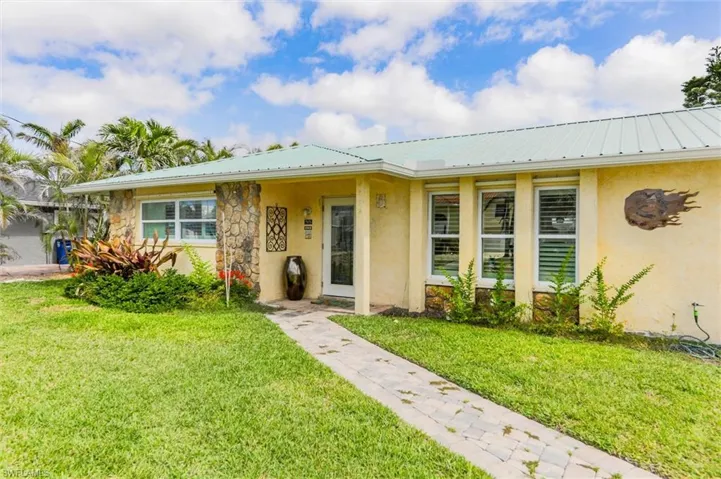 Single story home featuring metal roof, stucco siding, stone siding, and a front lawn