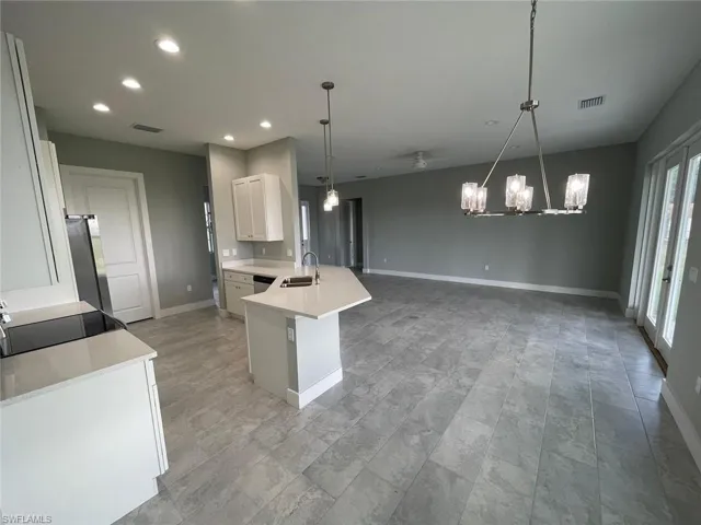 Kitchen with white cabinetry, ceiling fan with notable chandelier, appliances with stainless steel finishes, pendant lighting, and sink