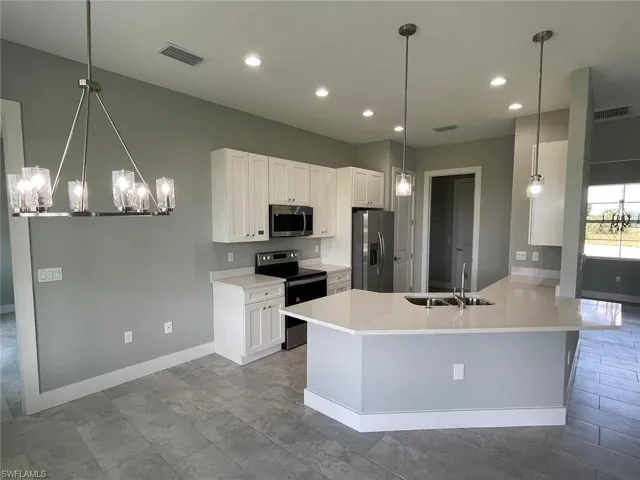 Kitchen featuring light tile floors, hanging light fixtures, sink, white cabinets, and appliances with stainless steel finishes