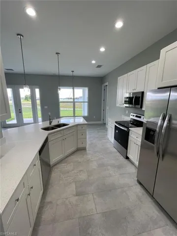 Kitchen with decorative light fixtures, light tile floors, sink, white cabinets, and appliances with stainless steel finishes