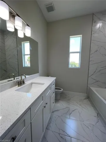 Full bathroom with a wealth of natural light, tile flooring, large vanity, and toilet