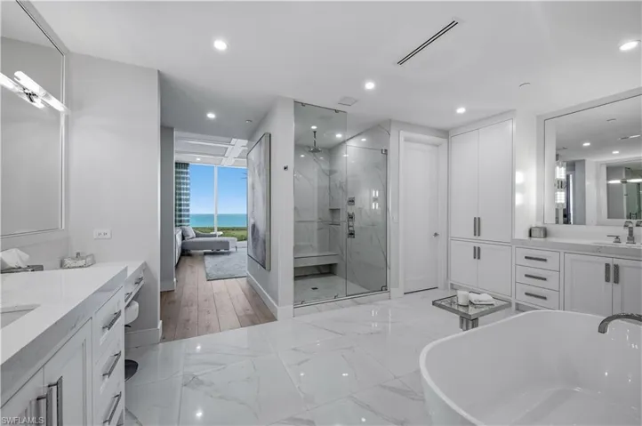 Bathroom featuring two vanities, a freestanding tub, a marble finish shower, light marble finish flooring, and recessed lighting