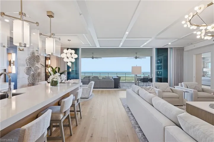 Living area with suspended lighting, expansive windows, light wood-style flooring, and beamed ceiling