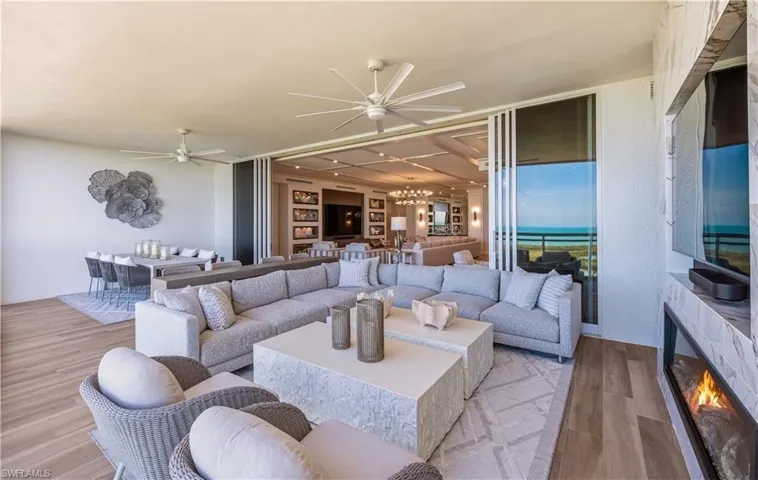 Living room featuring ceiling fan, wood finished floors, hanging lights, a lit fireplace, and built in features