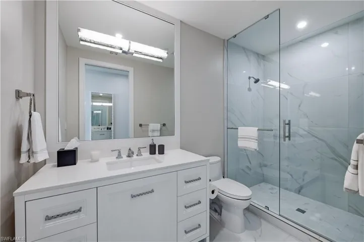 Bathroom with vanity, a marble finish shower, marble look tiles, and recessed lighting