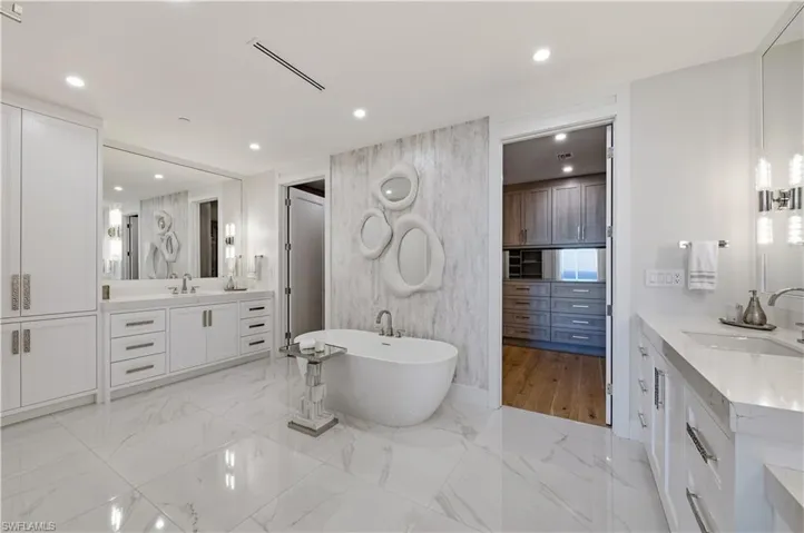 Bathroom with two vanities, a freestanding bath, recessed lighting, and light marble finish flooring