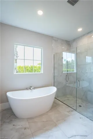 Full bathroom with marble look tile flooring, a freestanding tub, a marble finish shower, and recessed lighting