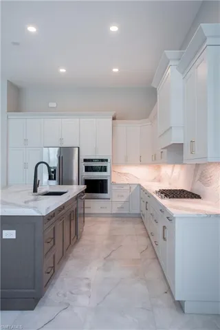 Kitchen with light marble finish floors, backsplash, white cabinetry, stainless steel appliances, and light stone counters