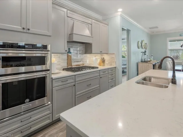Kitchen with custom range hood, appliances with stainless steel finishes, decorative backsplash, and an inviting island with seating to entertain in this open concept newer construction home