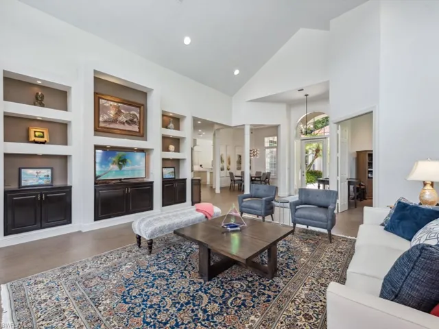 Living room featuring built in shelves, wood-type flooring, ornate columns, and high vaulted ceiling