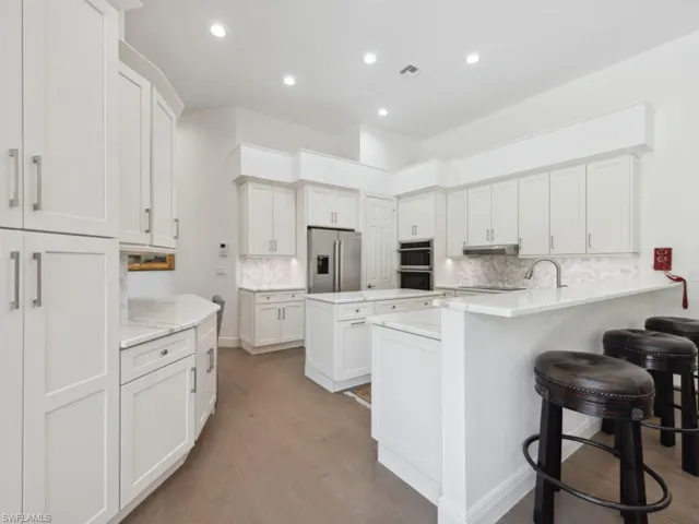 Kitchen with backsplash, appliances with stainless steel finishes, white cabinetry, and breakfast bar