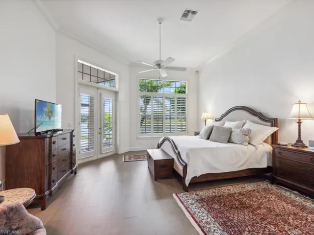 Primary bedroom featuring access to rear lanai, ceiling fan, crown molding, hardwood / wood-style floors, and french doors