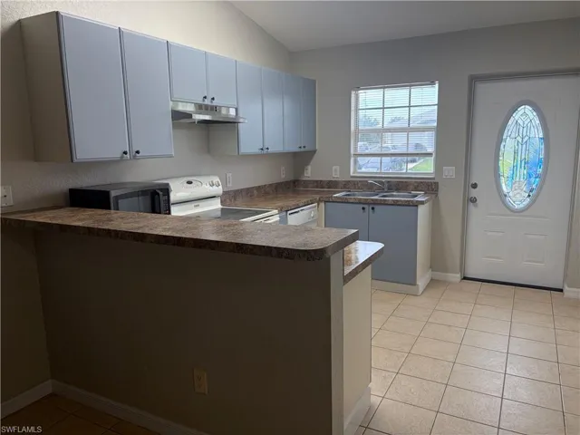 Kitchen featuring light blue cabinetry, mottled brown countertops, a double basin sink, and tile flooring