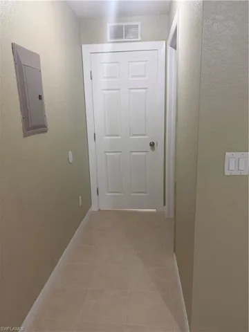 Hallway with light beige wall paint, white baseboards, and light-colored square floor tiles