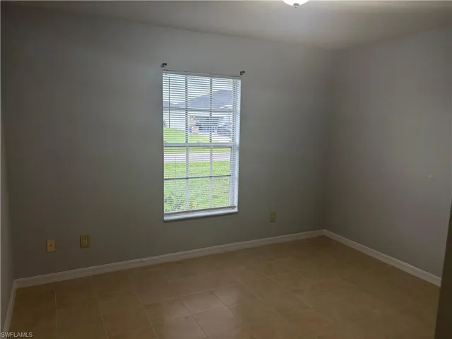 Neutral-toned room featuring a single window with horizontal blinds, light tan tile flooring, white baseboards, and a semi-flush mount ceiling light fixture