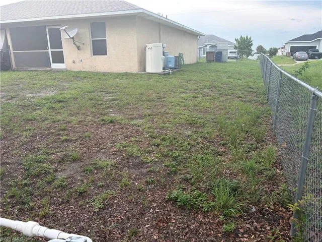 Expansive backyard featuring a partial chain-link fence, a screened patio with a white door, and a light-colored exterior wall with a window