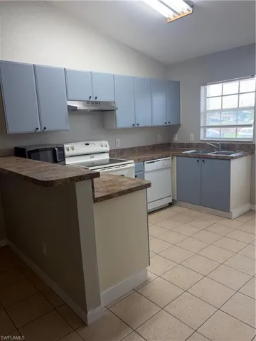 Kitchen with blue cabinetry, L-shaped laminate countertops, and a tile floor