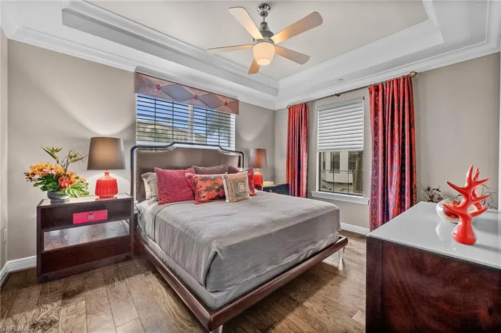 Bedroom with crown molding, a raised ceiling, hardwood / wood-style flooring, multiple windows, and a ceiling fan