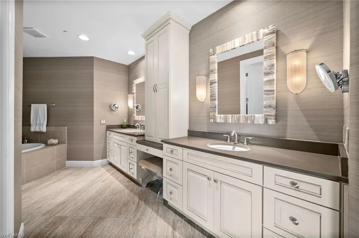 Full bath featuring two vanities, tiled tub, and recessed lighting