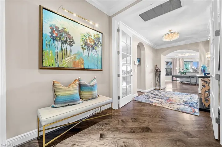Entrance foyer with arched walkways, crown molding, dark wood-style flooring, and a chandelier