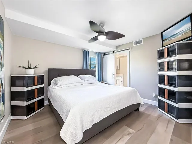 Bedroom featuring connected bathroom, a barn door, ceiling fan, and hardwood / wood-style floors