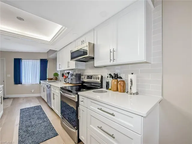 Kitchen featuring white cabinets, light wood-type flooring, stainless steel appliances, and tasteful backsplash