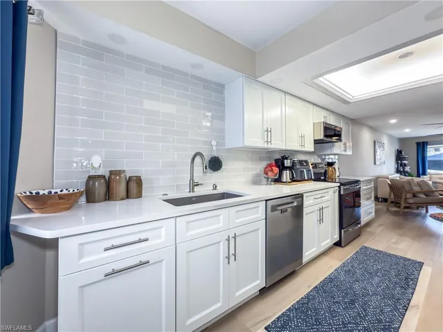 Kitchen with sink, appliances with stainless steel finishes, decorative backsplash, white cabinets, and light wood-type flooring