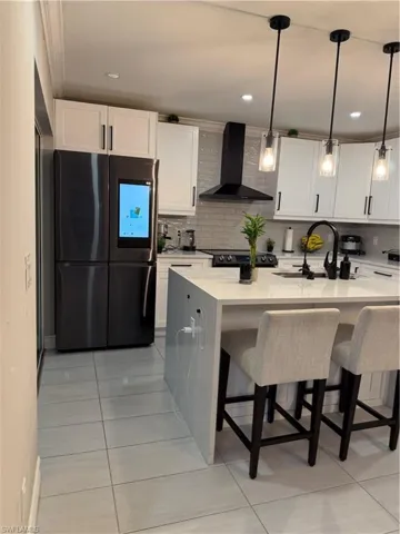 Kitchen featuring fridge, a breakfast bar, ventilation hood, light stone counters, and pendant lighting