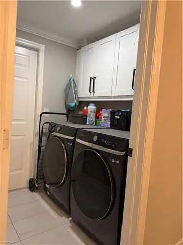 Washroom with cabinet space, crown molding, washer and dryer, and light tile patterned flooring