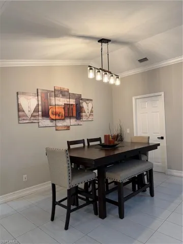 Dining room with crown molding, vaulted ceiling, and light tile patterned flooring