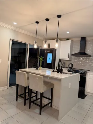 Kitchen featuring a center island with sink, ventilation hood, white cabinetry, range, and crown molding