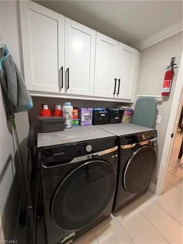 Laundry room with cabinet space, washing machine and clothes dryer, light tile patterned floors, and ornamental molding