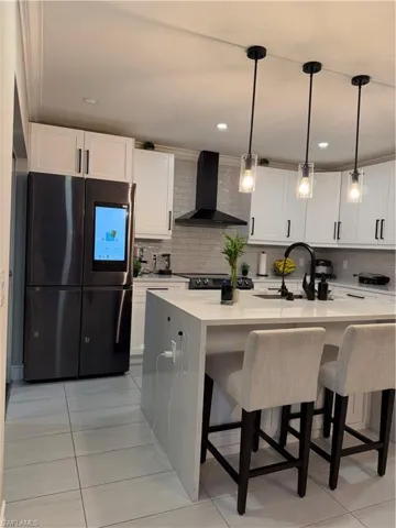 Kitchen featuring fridge, a breakfast bar, decorative light fixtures, extractor fan, and light stone countertops