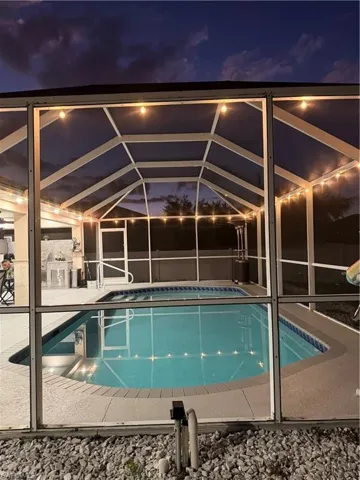 Pool at night featuring glass enclosure, an outdoor pool, a sunroom, and a patio