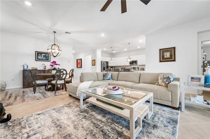 Living room featuring light tile patterned flooring, ceiling fan with notable chandelier, and ornamental molding