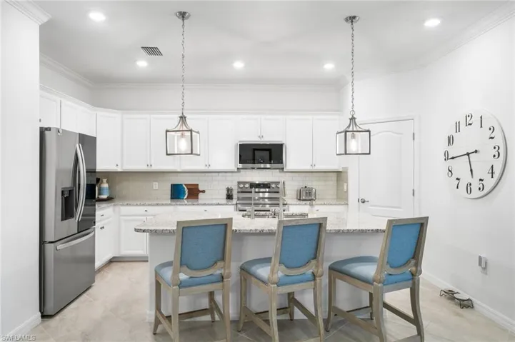 Kitchen with backsplash, stainless steel appliances, a center island with sink, and decorative light fixtures