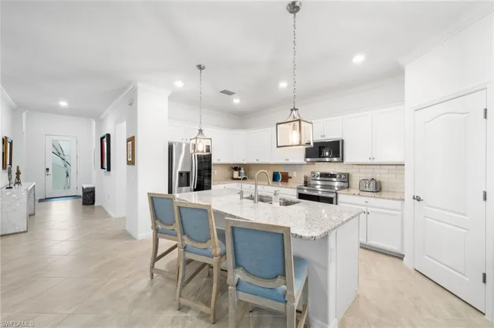 Kitchen with backsplash, sink, appliances with stainless steel finishes, light stone countertops, and white cabinets
