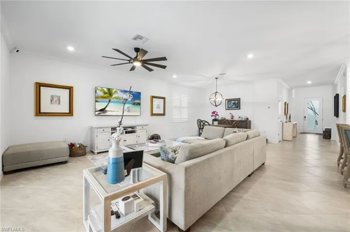 Living room with ceiling fan with notable chandelier, crown molding, and light tile patterned floors