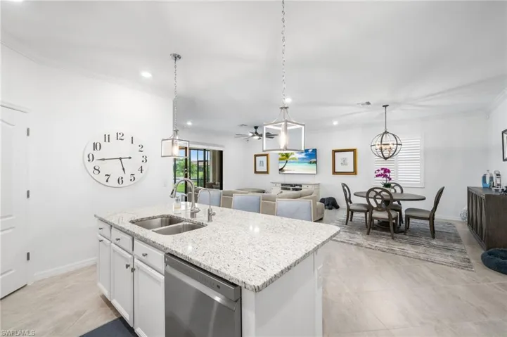 Kitchen with stainless steel dishwasher, white cabinets, light stone countertops, sink, and a center island with sink